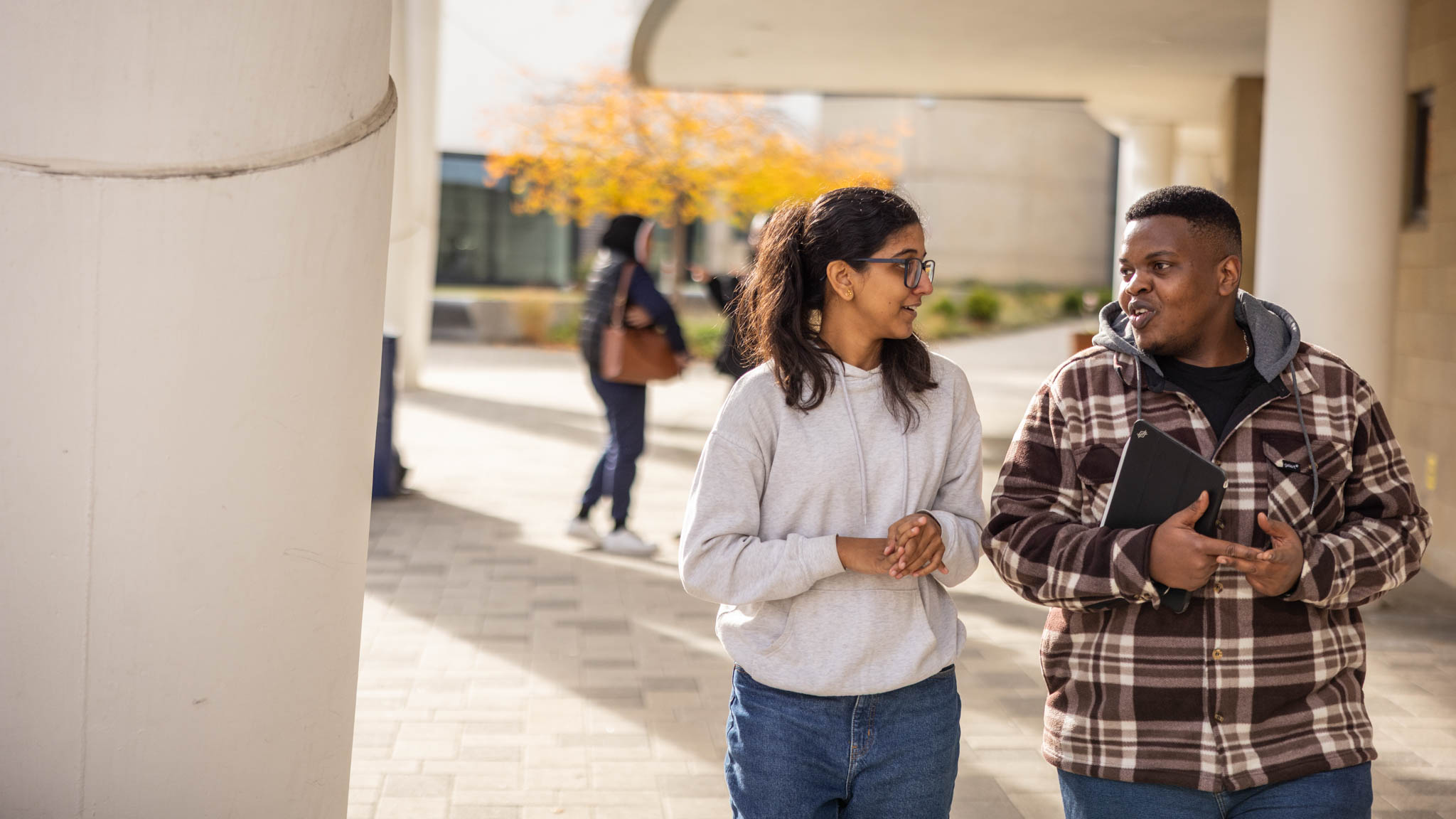Two students walking round campus and talking to each other