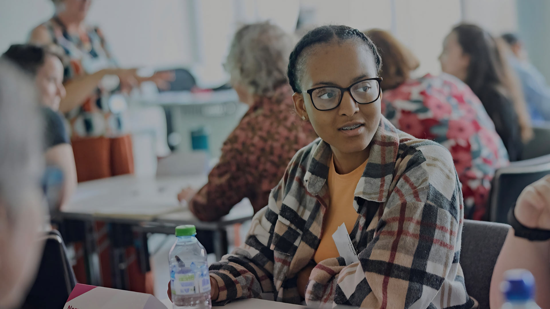 Acacia sat a table with a pen in her hand and a water bottle in front of her.