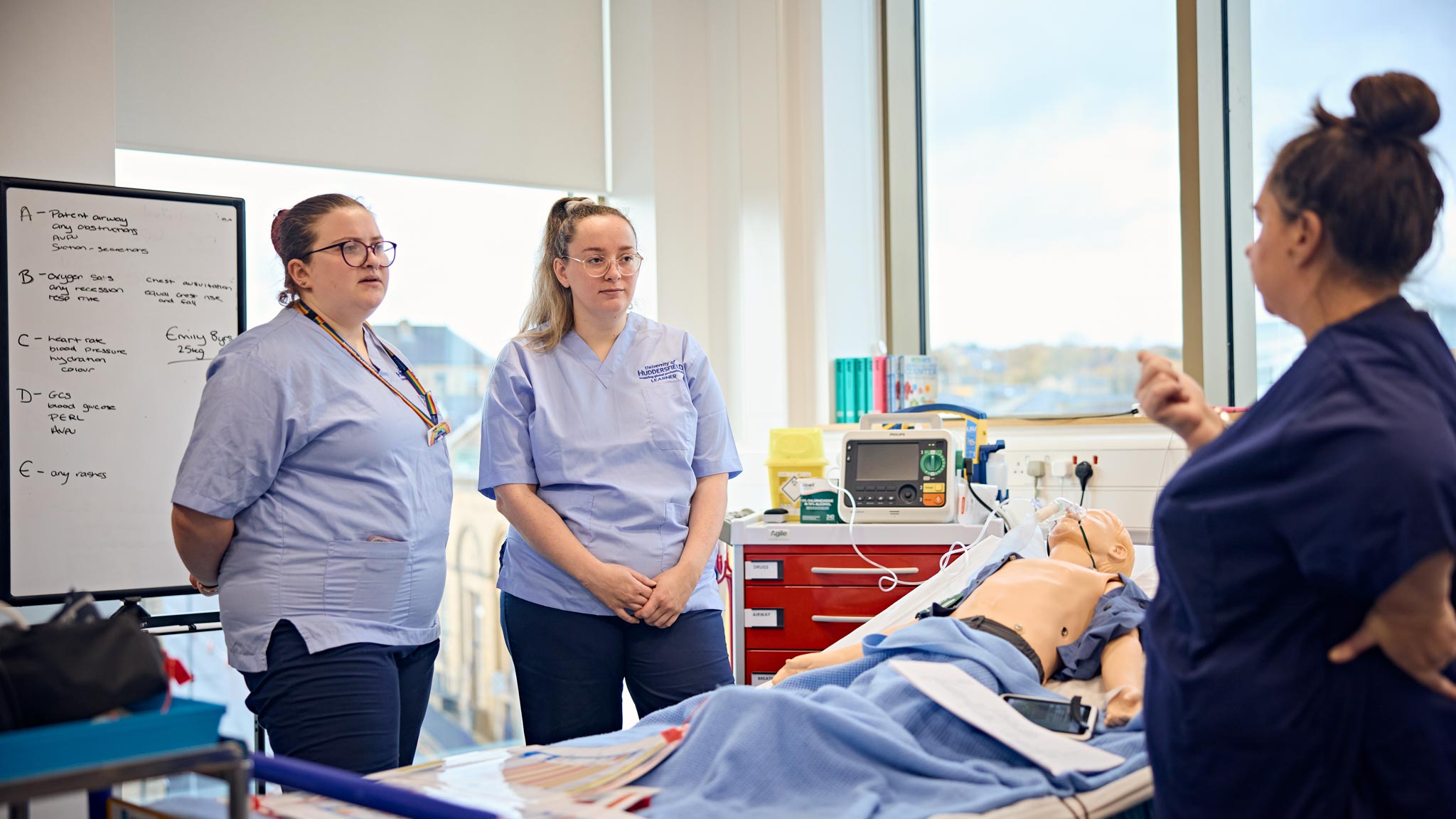 Two students learning in a hospital simulator being taught by a lecturer