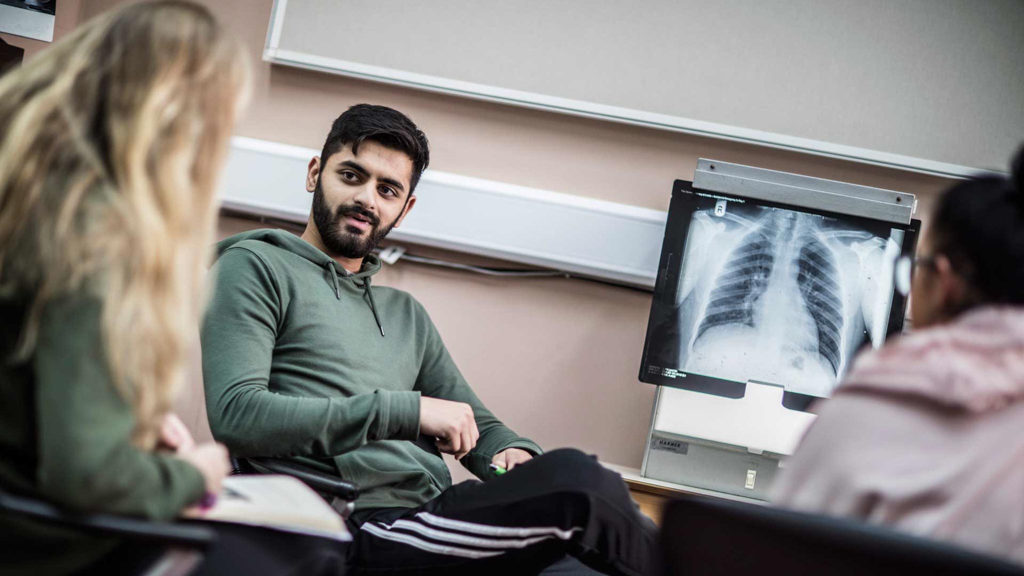 A man talking with a chest x ray in the background